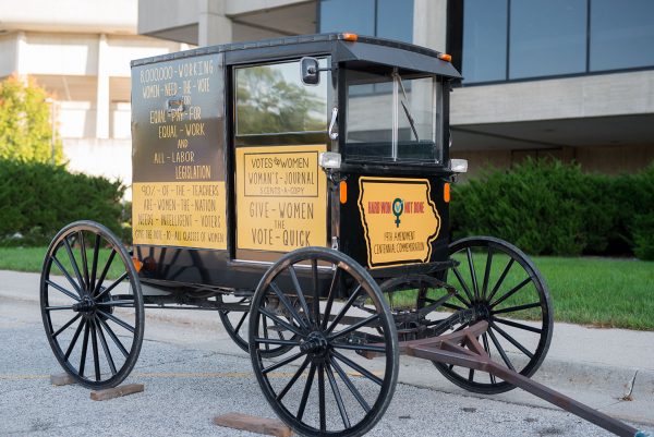 Replica of a suffrage wagon used in the late 19th century, sitting in front of the Scheman Building. The wagon is painted with suffrage slogans.