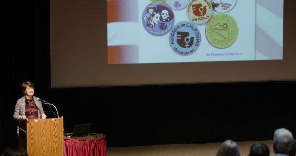 Marjorie Spruill standing at the podium during her lecture in Benton Auditorium. A slide from her presentation is visible on the screen.