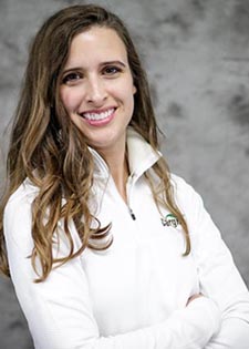 Maggie Luttrell Roby - head-and-shoulders photo of a white women with long brown hair wearing a white 3/4 zip pullover with a Cargill logo, standing with her arms crossed over her chest