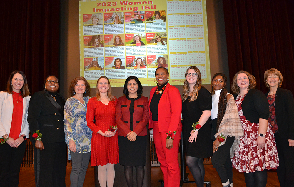 Ten of the twelve 2023 Women Impacting ISU calendar honorees stand in front of the stage, with an image of the calendar displayed on the screen behind them.