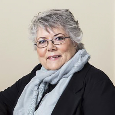 Head-and-shoulders photo of Sally Roesch Wagner, a middle-aged women with short gray hair and dark-rimmed glasses, wearing a dark top and blazer and a light gray scarf.